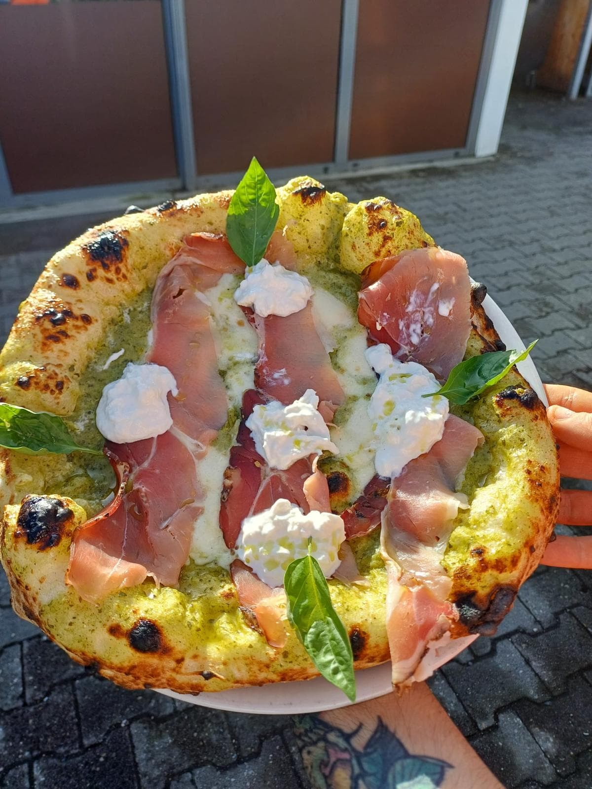 Pizza mit Pesto, Rohschinken und Burrata, draußen in der Hand gehalten