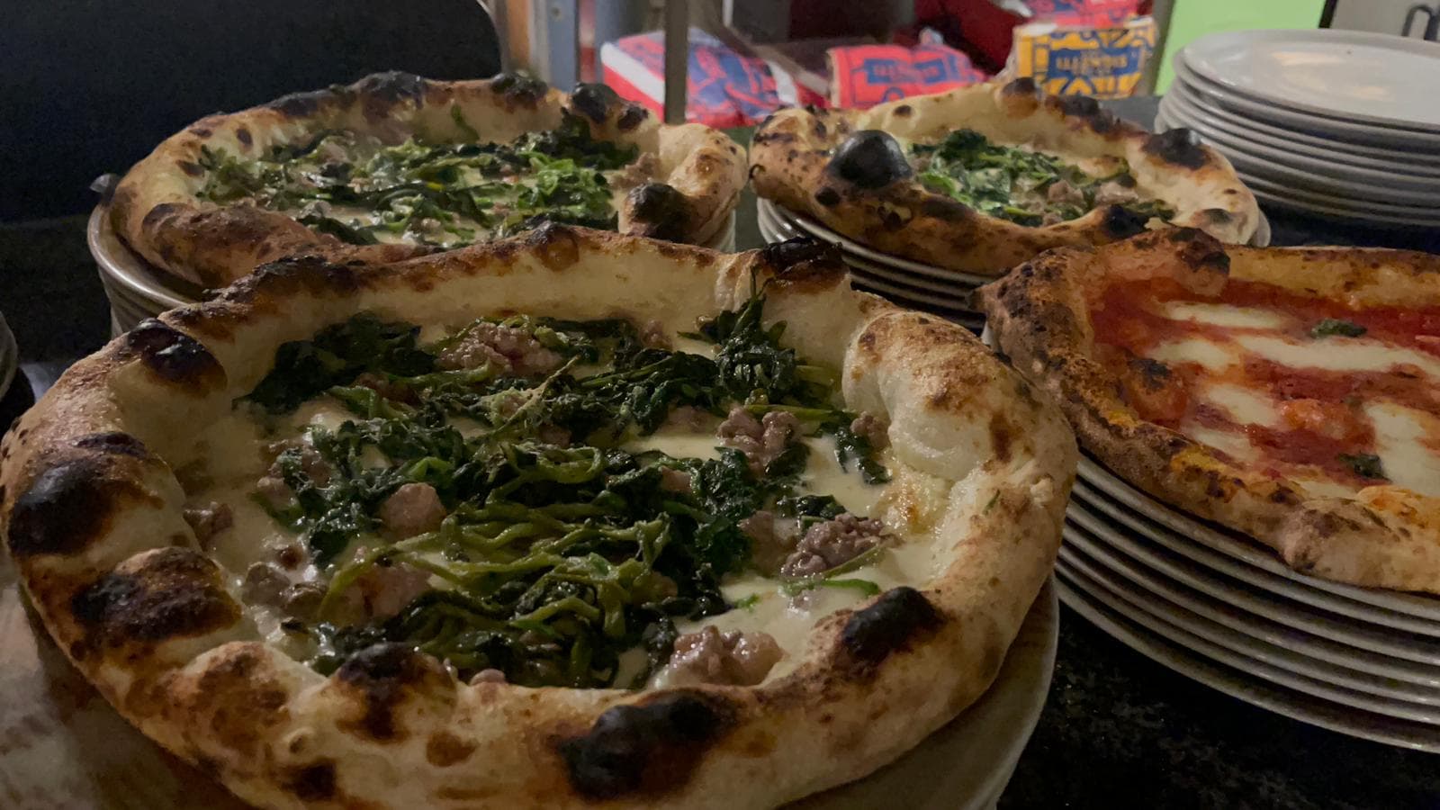 Mehrere frisch gebackene Pizzen mit dunkel geflecktem Rand auf gestapelten Tellern